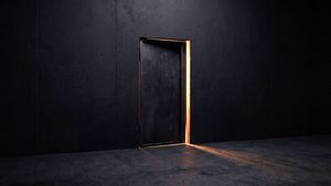 Eine geschlossene dunkle Wand mit einer Tür, die einen Spalt offen steht, warmes Licht fällt als schmaler Keil auf den Boden