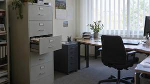Büro einer kleinen Steuerkanzlei mit gemeinsamem Aktenschrank, eine Schublade mit Hängeregistern offen, daneben ein Rollcontainer