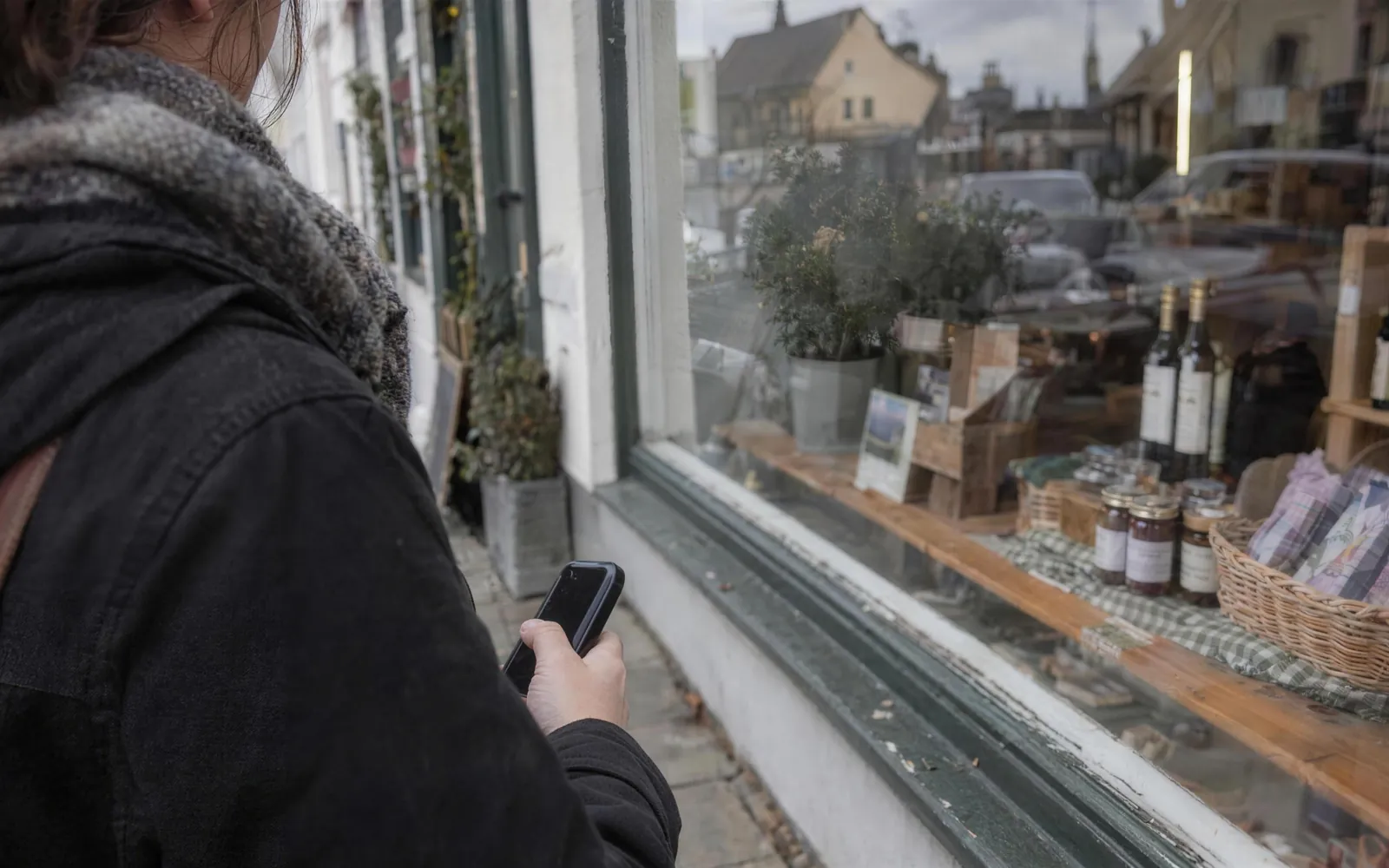 Eine Person mit Handy in der Hand steht vor dem Schaufenster eines kleinen Ladens